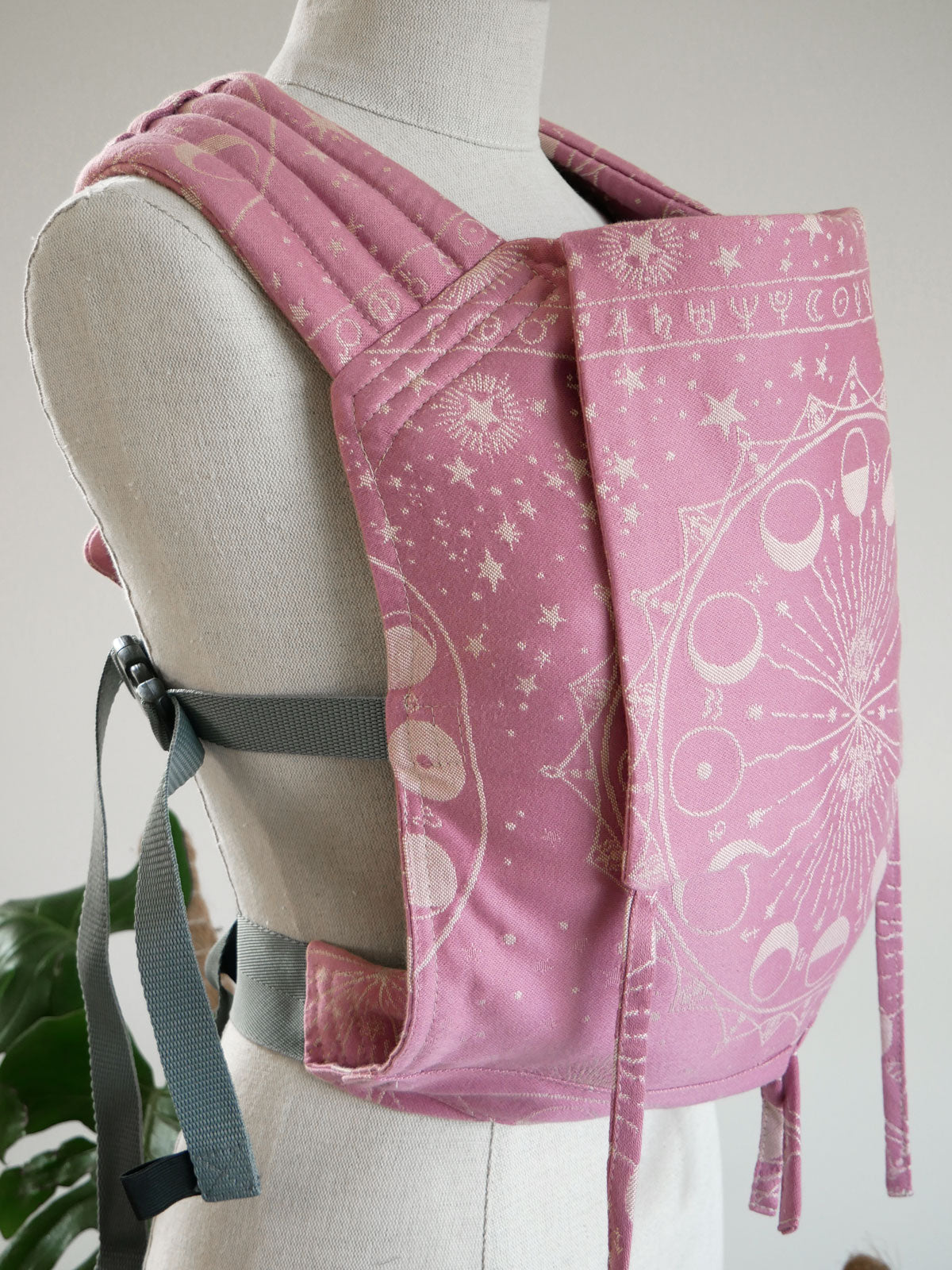 Pink baby carrier with celestial patterns on a mannequin against a neutral background