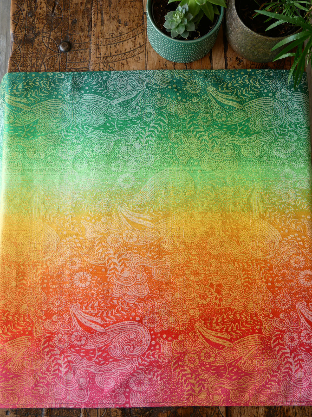 Colourful patterned Marina Starburst Baby Wrap on a wooden surface with plants.