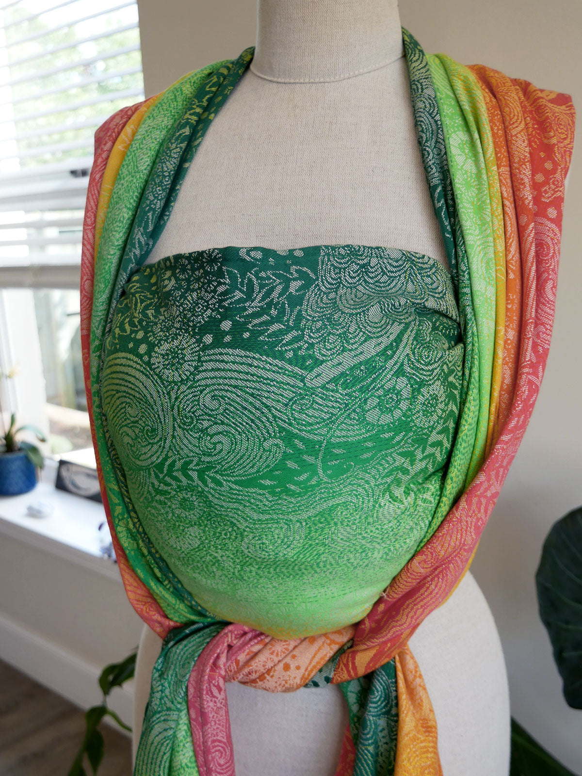 Mannequin wearing a colorful Marina Starburst Baby Wrap with a green patterned top.