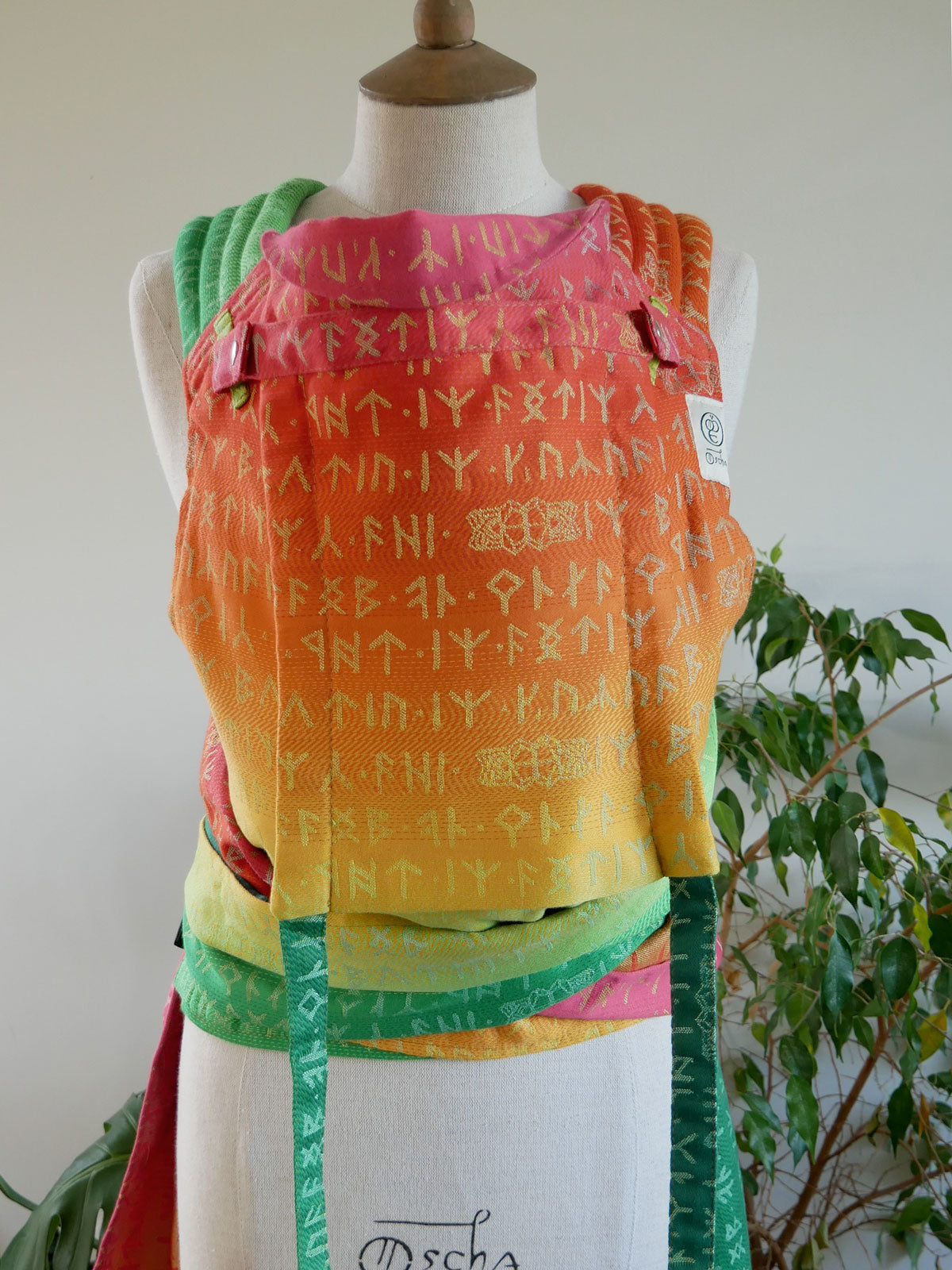 Colorful baby carrier with text pattern on a mannequin against a neutral background