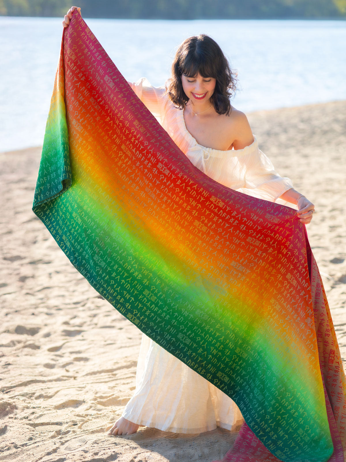 Woman holding a colorful gradient woven wrap on a beach