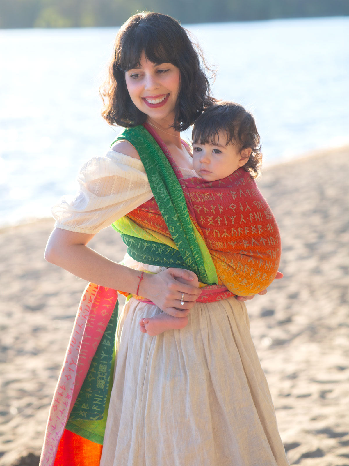 Woman holding a child on a beach with a colourful Moria Citrus Baby Wrap