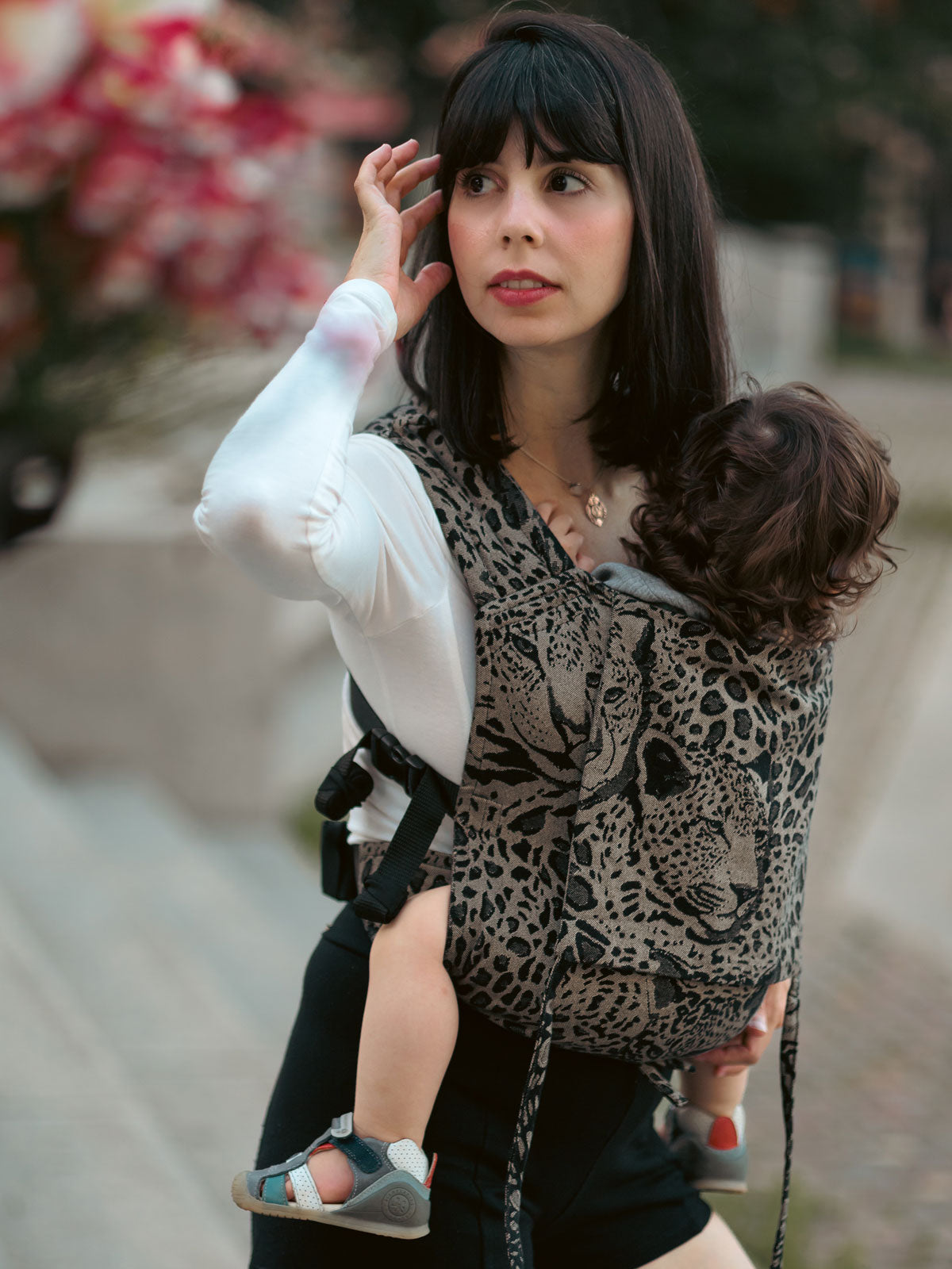 Woman carrying a child in a leopard print Prowl Savannah Bairn Baby Carrier outdoors.