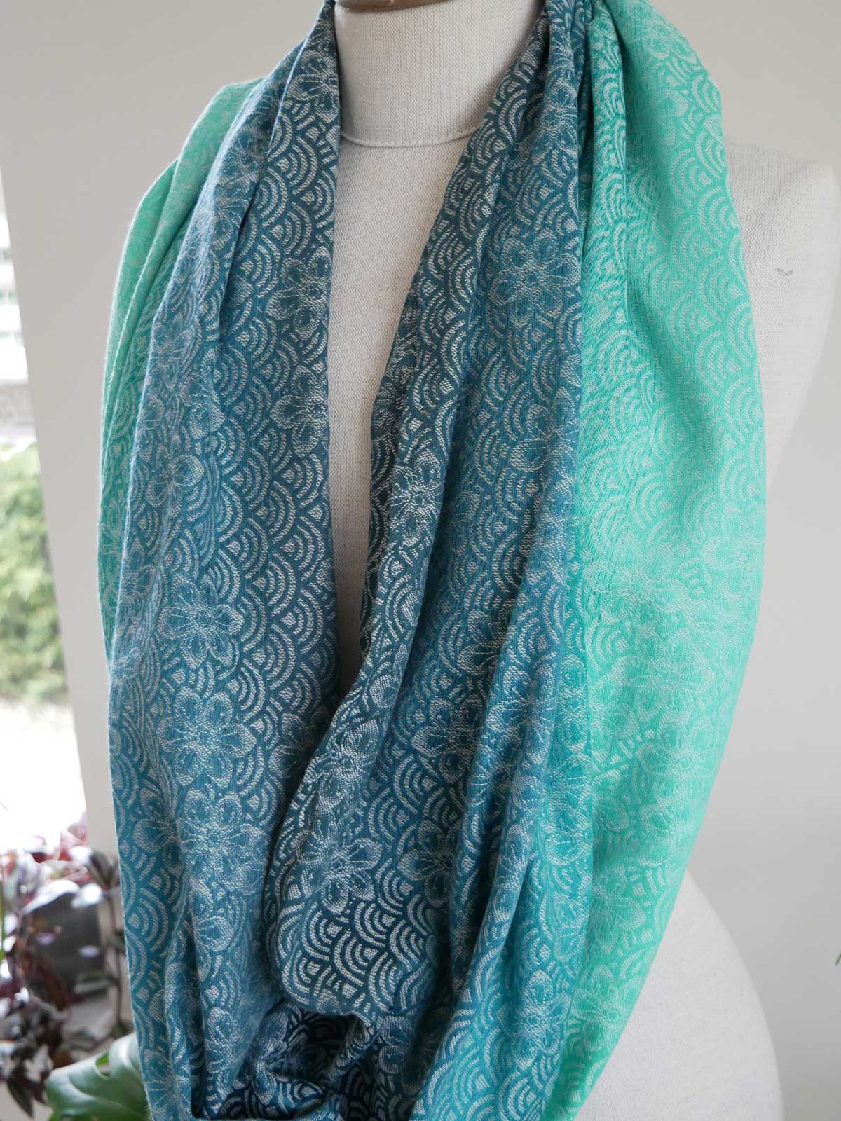 Teal patterned infinity loop on a mannequin with a blurred indoor background