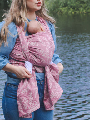 Woman holding a baby in a pink sling by a body of water