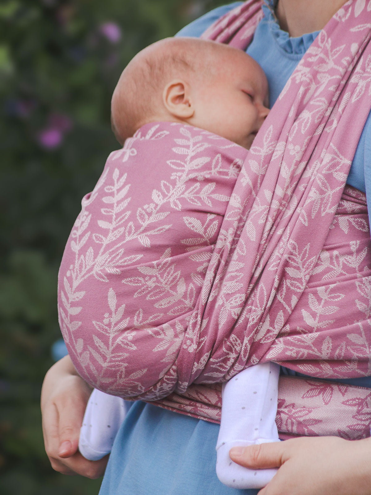Baby being carried in a floral pink baby wrap with a blurred green background